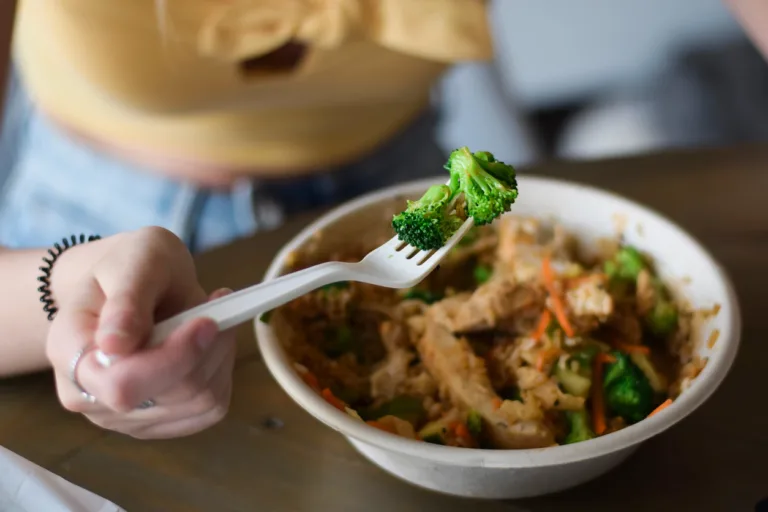 Young woman eating take out food with closeup on a broccoli on a plastic disposable single use fork