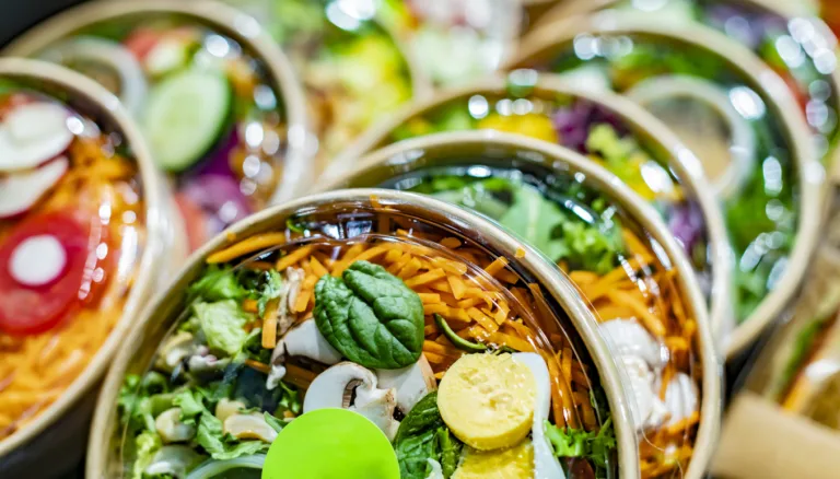 Pre-packaged vegetable salads in disposable packaging displayed in a commercial refrigerator